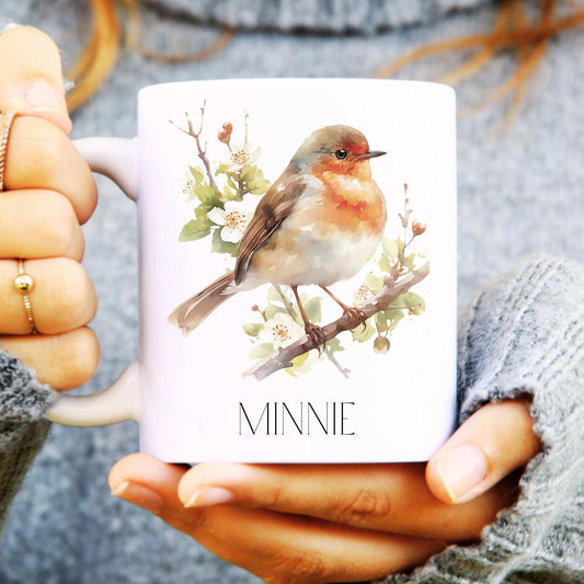 Person holding a mug with a robin design and 'Minnie' text