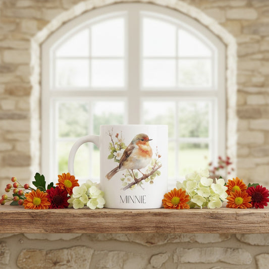 Mug with a robin design on a wooden shelf with flowers, against a stone wall and window background.