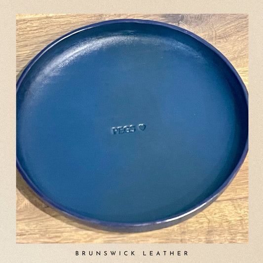 Blue leather tray with 'PEGS' branding on a wooden surface, branded 'Brunswick Leather'.