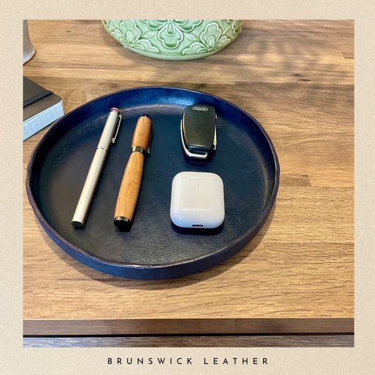 Blue leather tray with a pen, phone, and other items on a wooden surface, branded 'Brunswick Leather'.