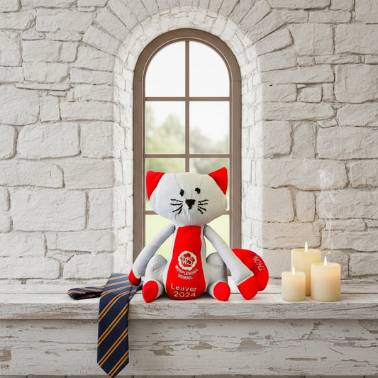 Stuffed toy cat with a red scarf and tie on a stone wall background