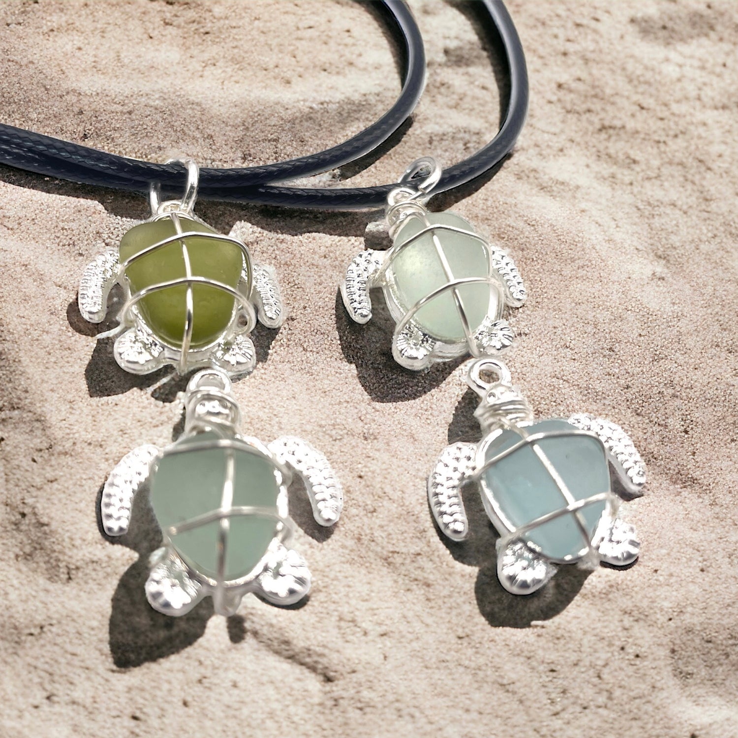  Four sea glass turtle necklaces on the sand.