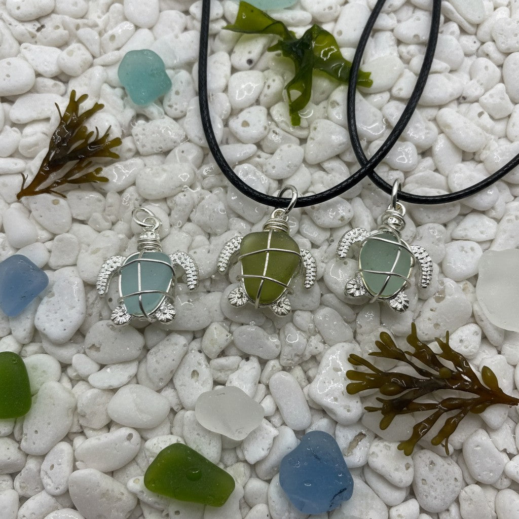 Three turtle-shaped necklaces with sea glass on a pebble and seaweed background