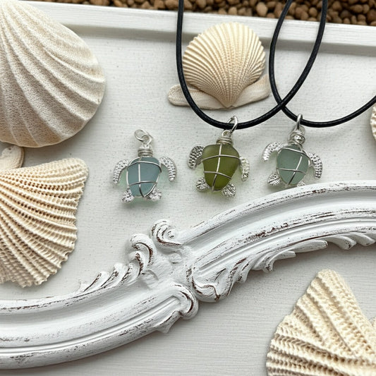 Three turtle-shaped necklaces with green stones on black cords, surrounded by seashells on a decorative white surface.