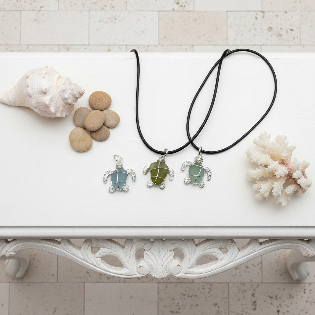 Three turtle-shaped pendants on black cords with seashells and coral on a white surface.