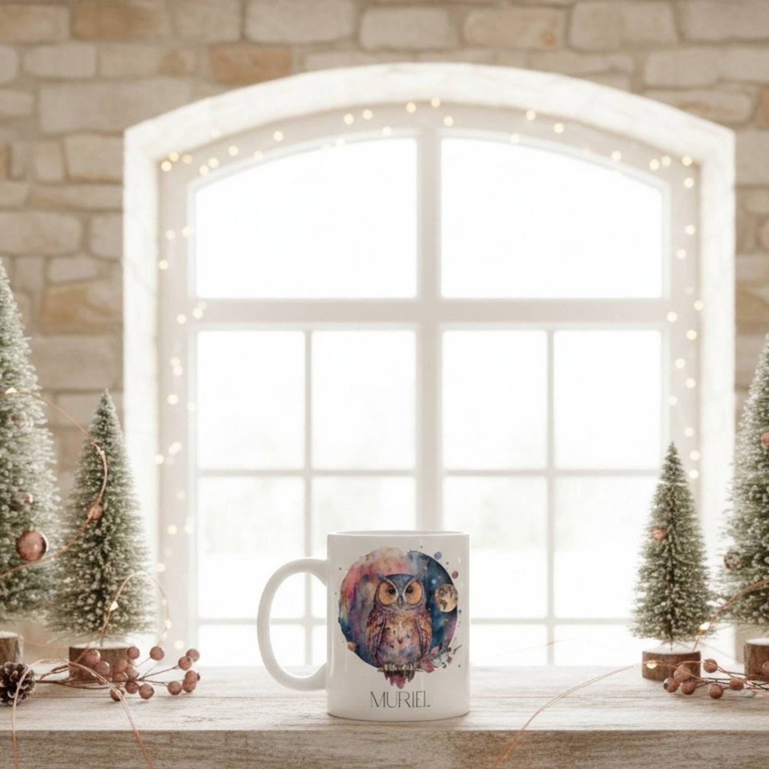 Mug with owl design on a windowsill with decorative trees and lights.