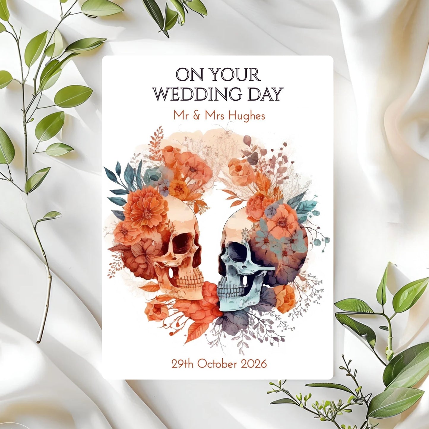 Wedding card with skull design and floral elements on a white fabric background
