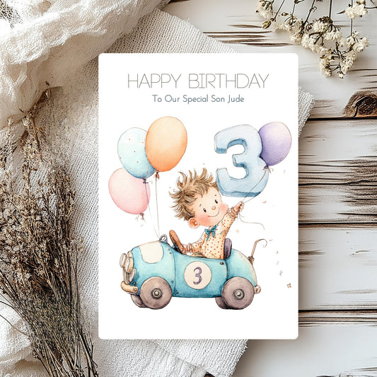 Birthday card with a child in a car and balloons, surrounded by decorative elements on a wooden surface.