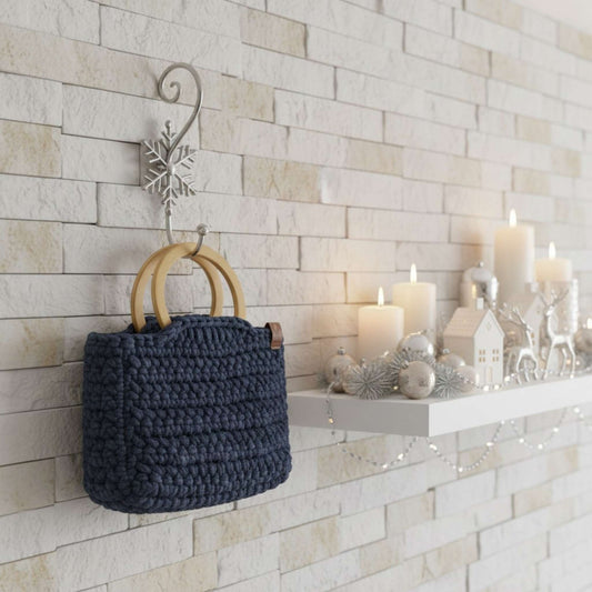 Navy blue woven bag hanging on a decorative wall hook with candles and small decorative items on a ledge.
