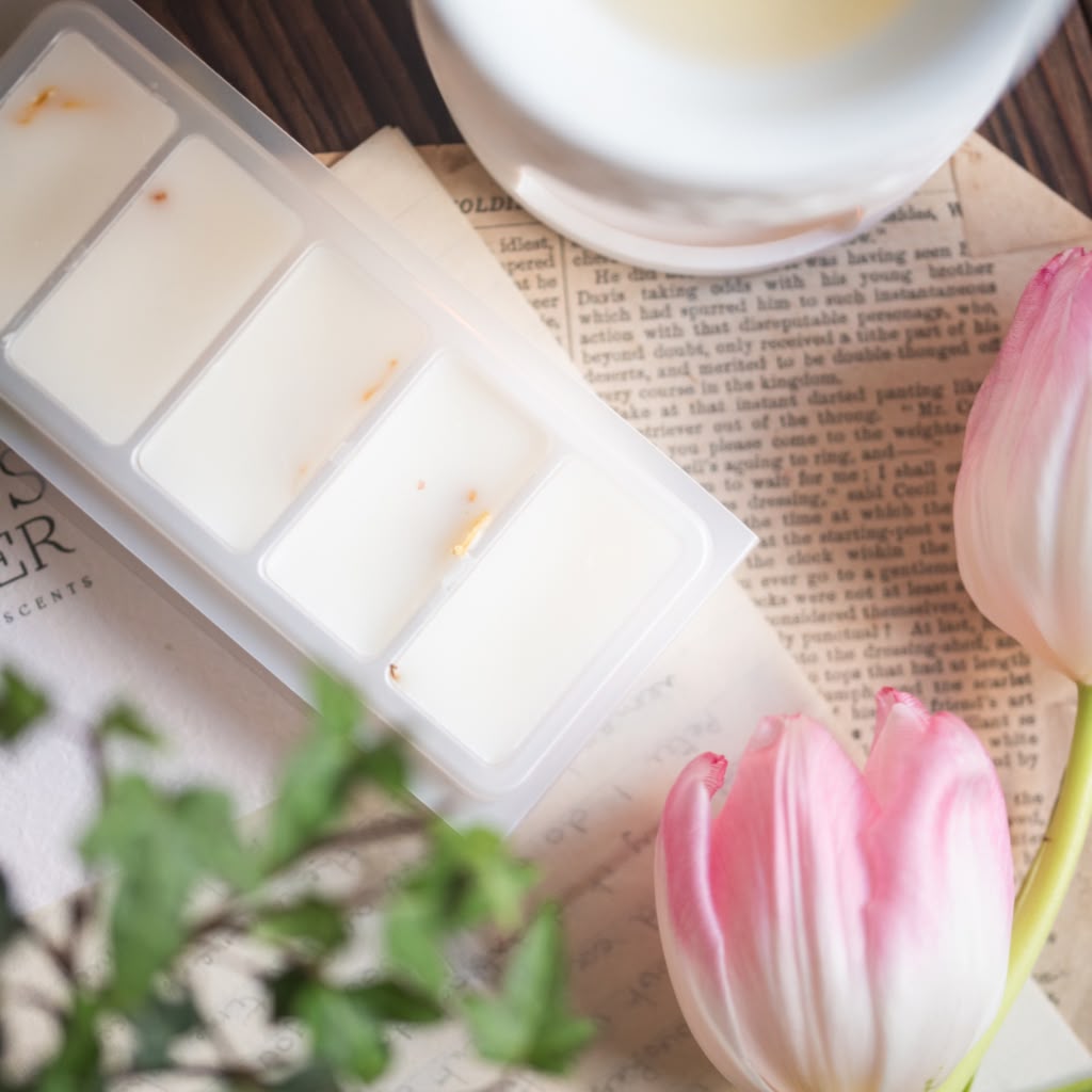 A clear plastic multi-compartment wax melt or soap tray containing white wax, styled on vintage book pages with pink tulips and green leaves.