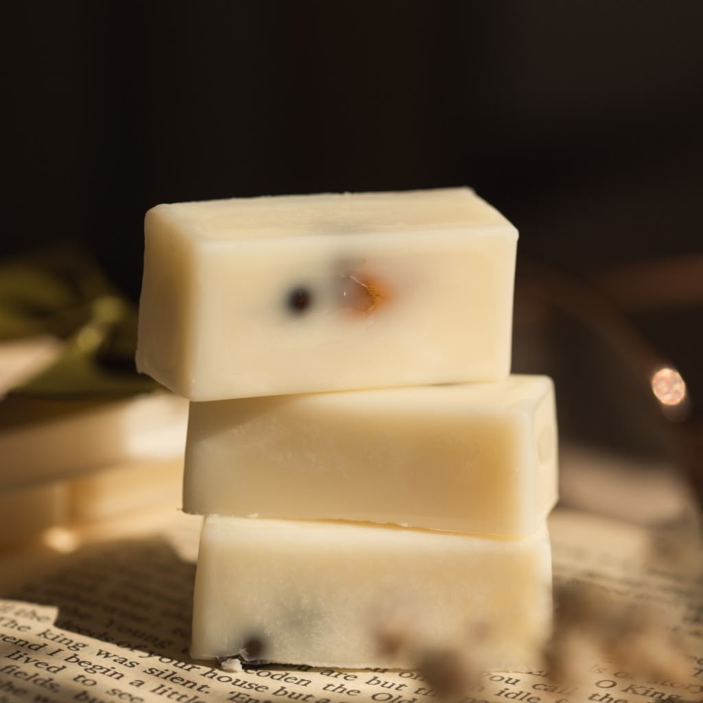 Three stacked rectangular bars of creamy off-white wax melts on a surface with printed text, softly lit with warm light and a blurred dark background.