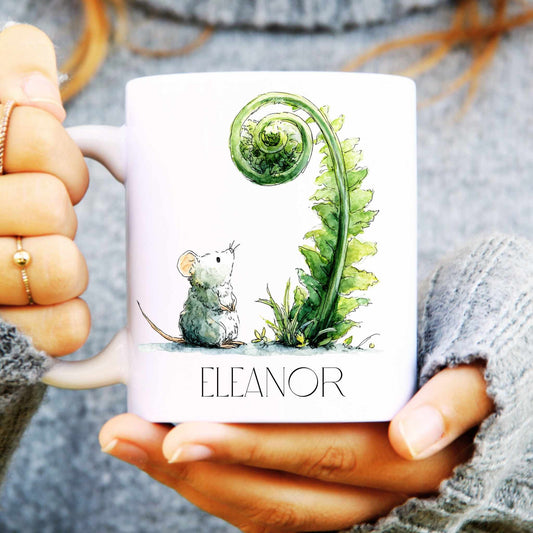 Person holding a mug with a design of a mouse and a plant, with 'Eleanor' printed on it.