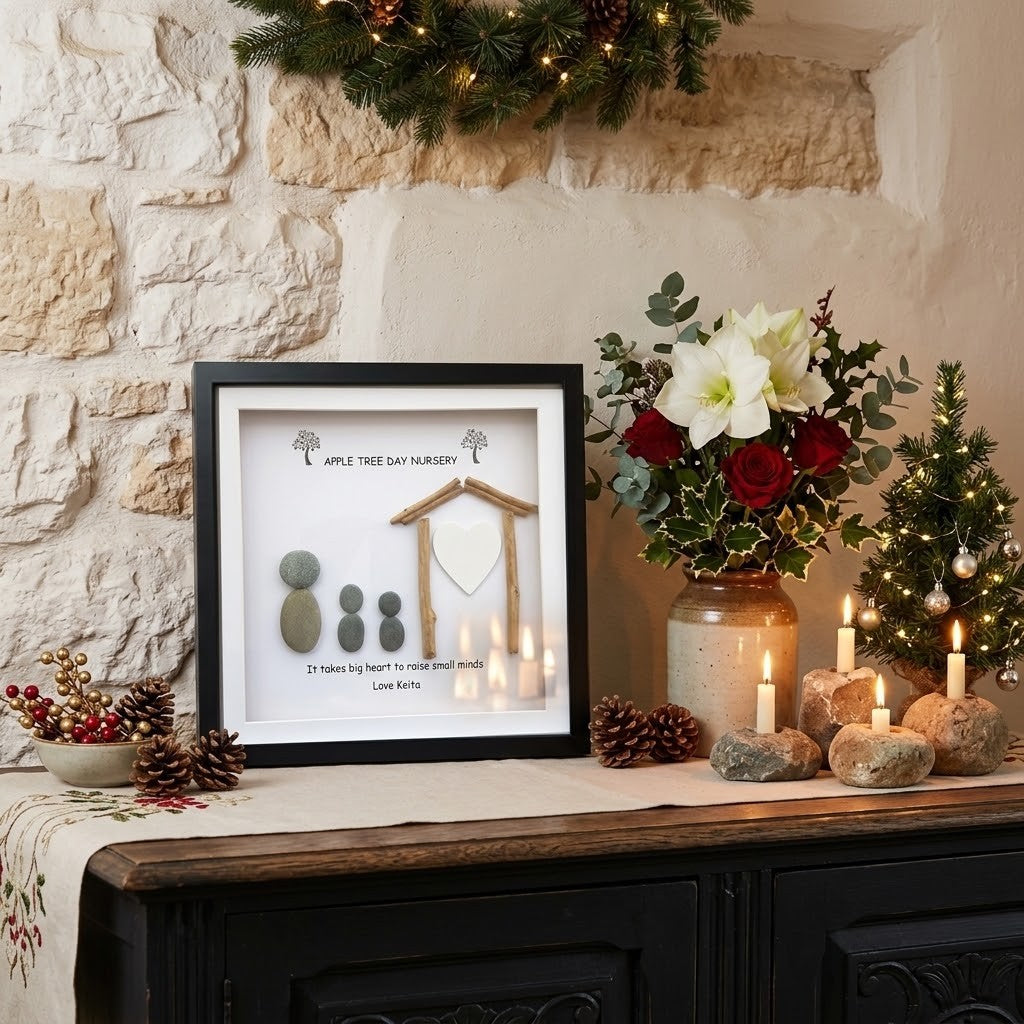 A framed personalised teacher keepsake print on a rustic wooden console table decorated for Christmas, featuring a black frame, white background, stone pavers, and a wooden treehouse silhouette. The background shows a stone wall, a garland, and holiday floral arrangements.