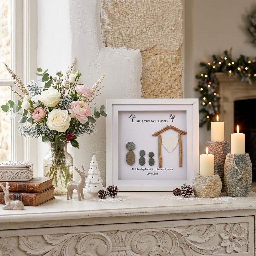 A framed teacher keepsake pebble art frame styled on a white carved mantelpiece alongside a floral arrangement, candles, pinecones, and small decorative figures in a warm, rustic interior setting.