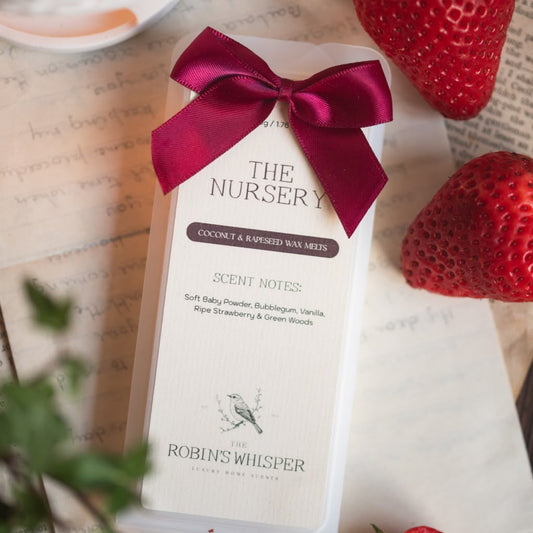 A wax melt package for The Nursery by The Robin's Whisper, tied with a dark red satin bow, displayed on a vintage book page with strawberries as props.