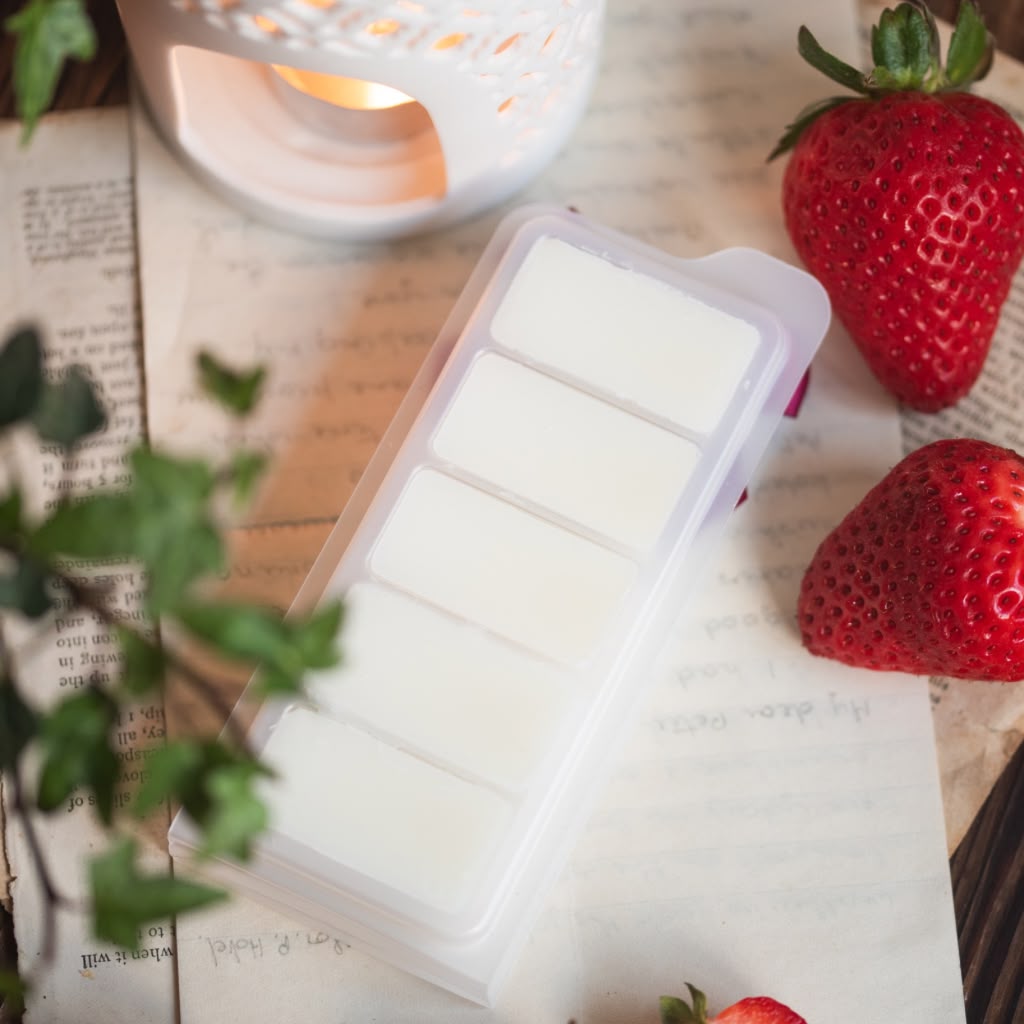 Wax melt bars in a mold with strawberries and a candle on an open book