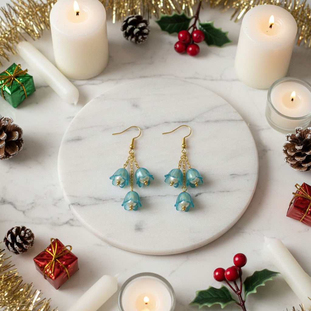 Pair of blue floral earrings on a marble surface with candles and Christmas decorations.
