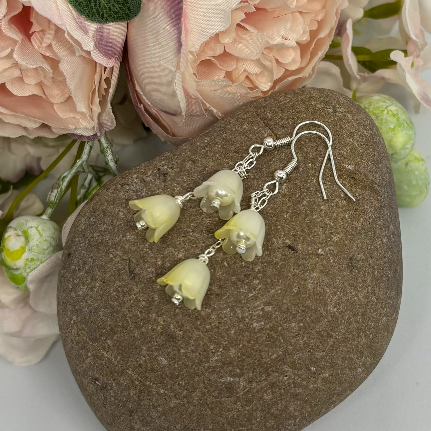 tulip earrings with silver hooks on a stone with floral elements behind.
