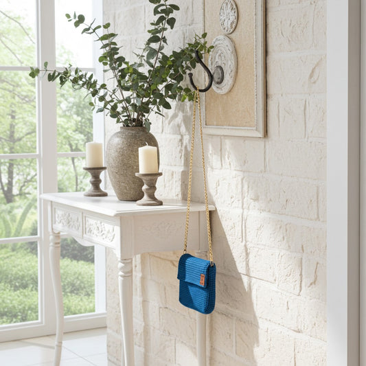 Turquoise phone handbag hanging on a wall hook next to a white console table with decor items.