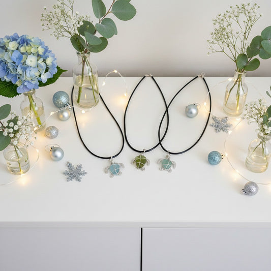 Three necklaces with charms on a white surface with decorative Christmas lights and flowers.