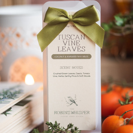 Pack of Tuscan Vine Leaves wax melts with a green bow, surrounded by tomatoes and a candle.