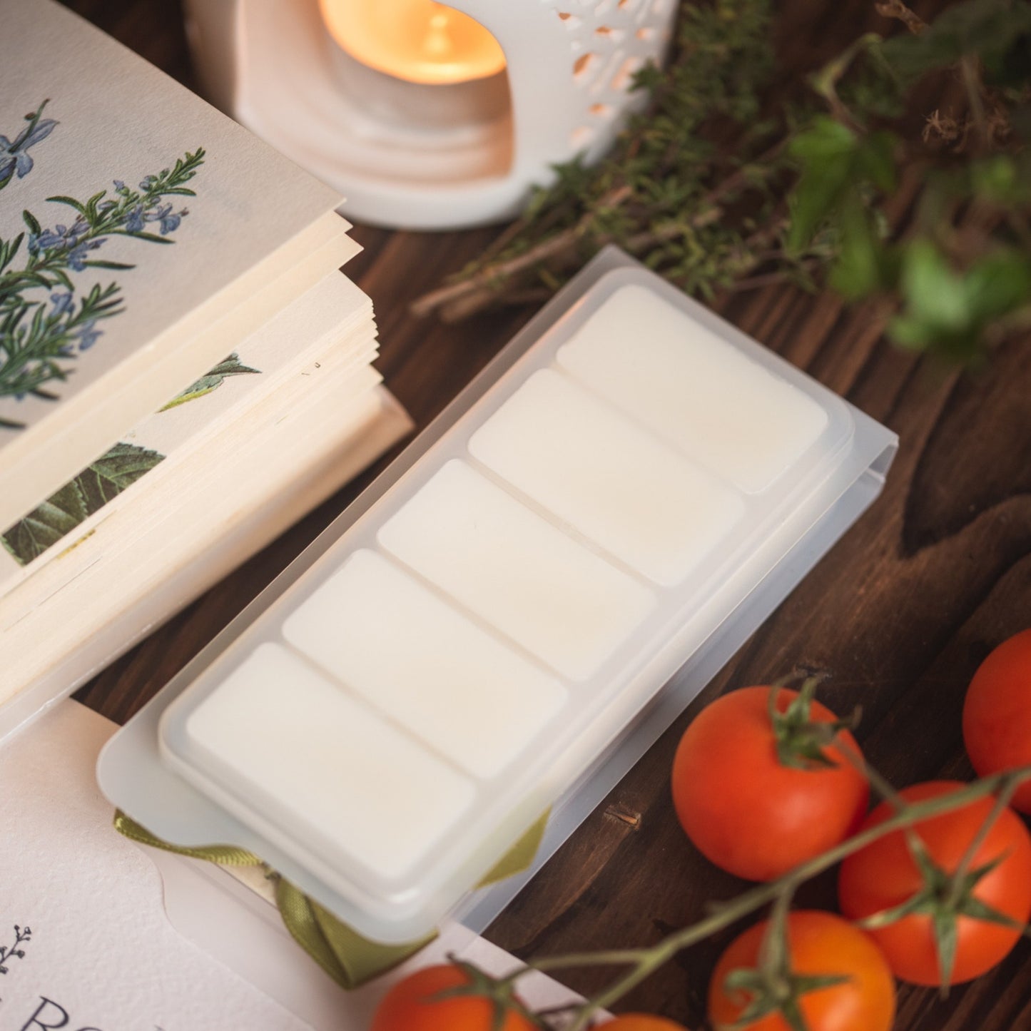 White wax melt bars in a mold on a wooden surface with tomatoes and a candle in the background