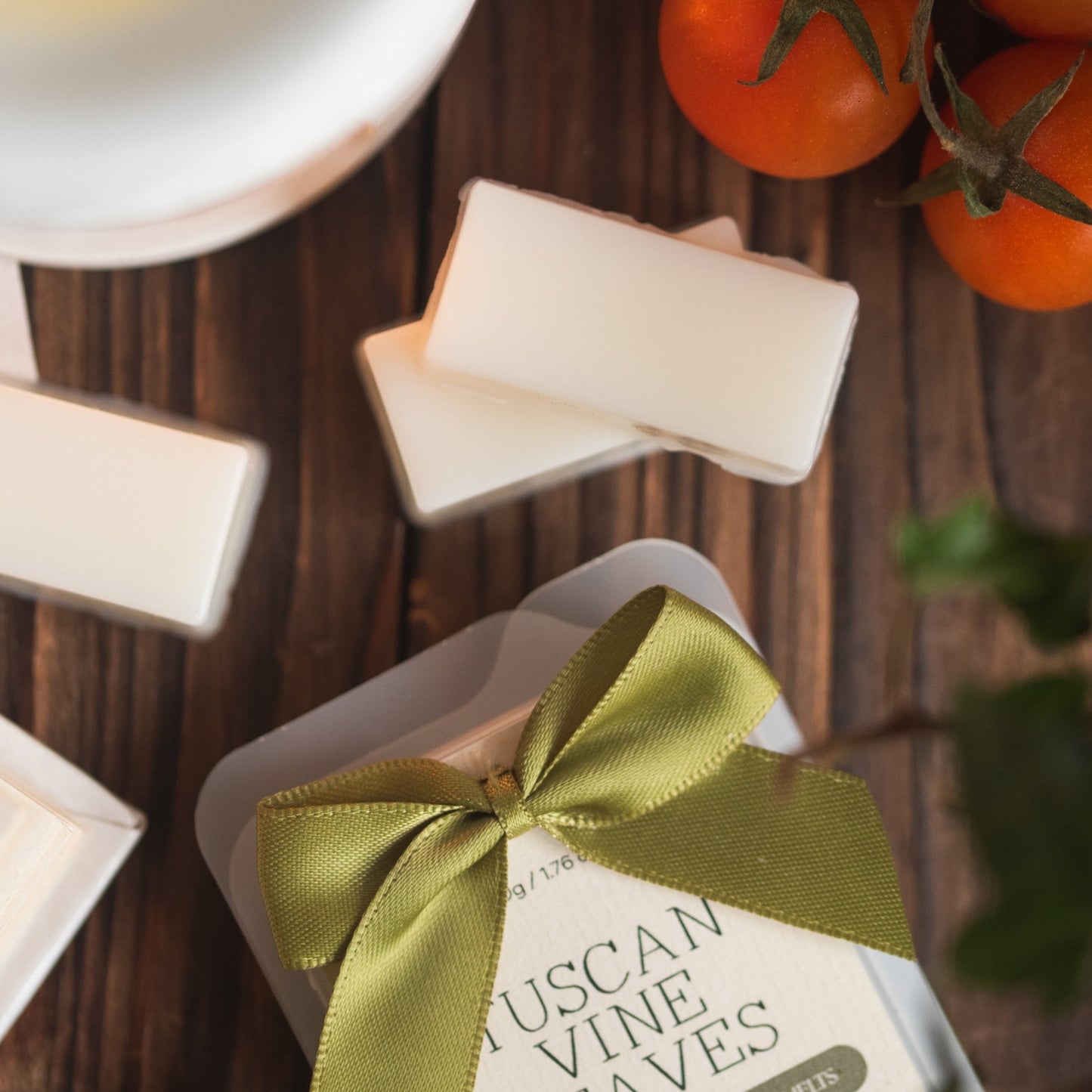 Wax melts with a green ribbon on a wooden surface with tomatoes in the background