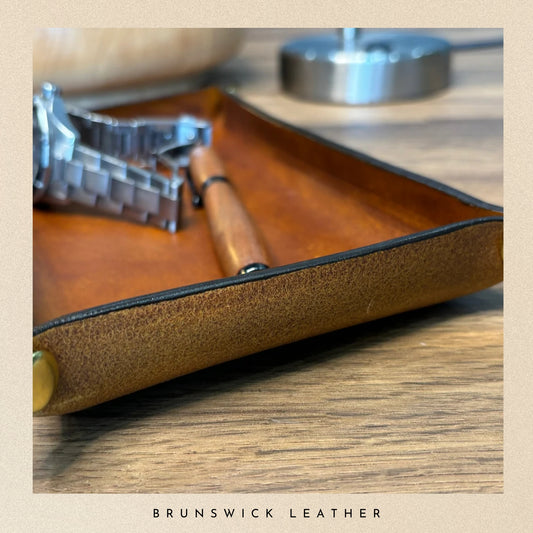 Brown leather tray with a pen and small tool on a wooden surface, branded 'Brunswick Leather'.