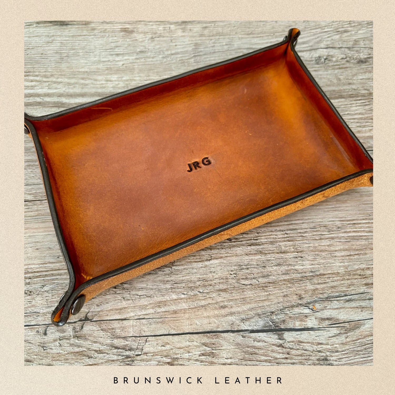 Brown leather tray with 'JRG' engraving on a wooden surface, branded 'Brunswick Leather'.