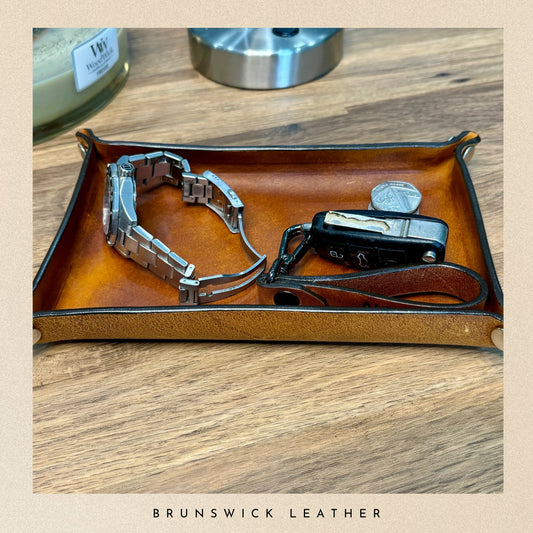 Brown leather tray with jewellery on a wooden surface, featuring 'Brunswick Leather' branding.