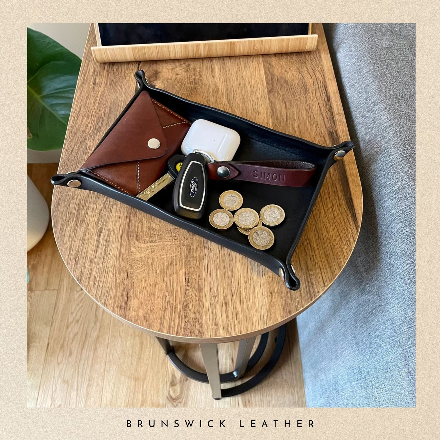 Black leather tray with accessories on a wooden table, featuring 'Brunswick Leather' branding.
