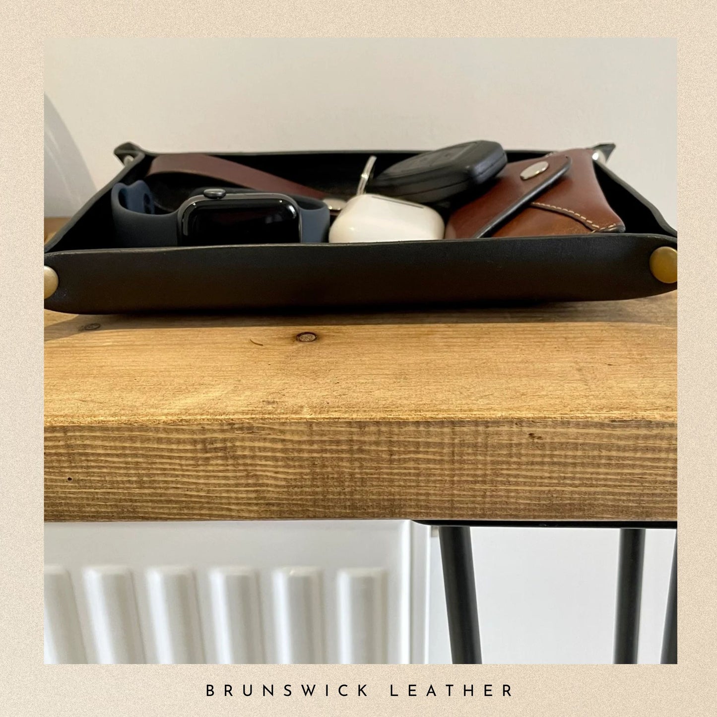 Black leather tray with items on a wooden surface, featuring 'Brunswick Leather' branding.