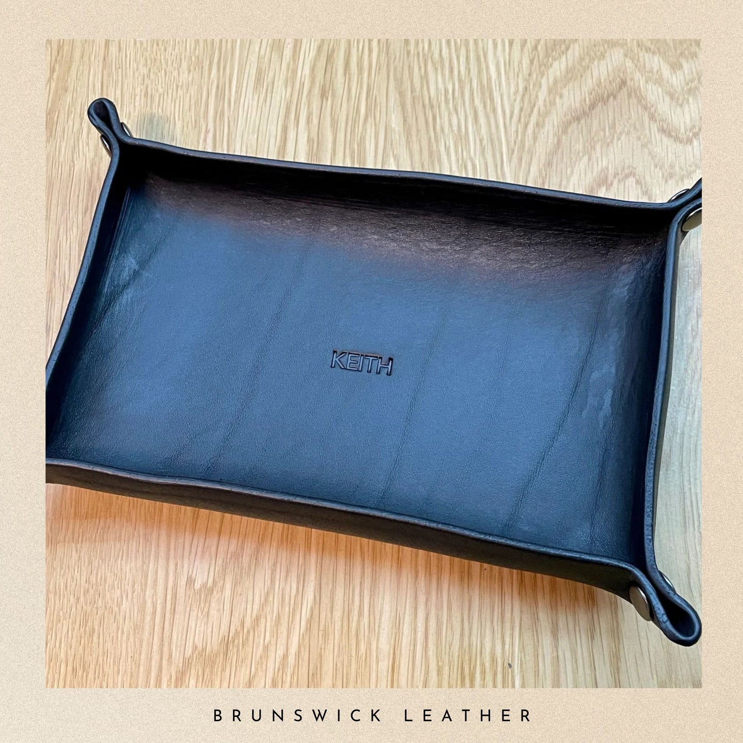 Blue leather tray with 'Keith' branding on a wooden surface, branded 'Brunswick Leather'.