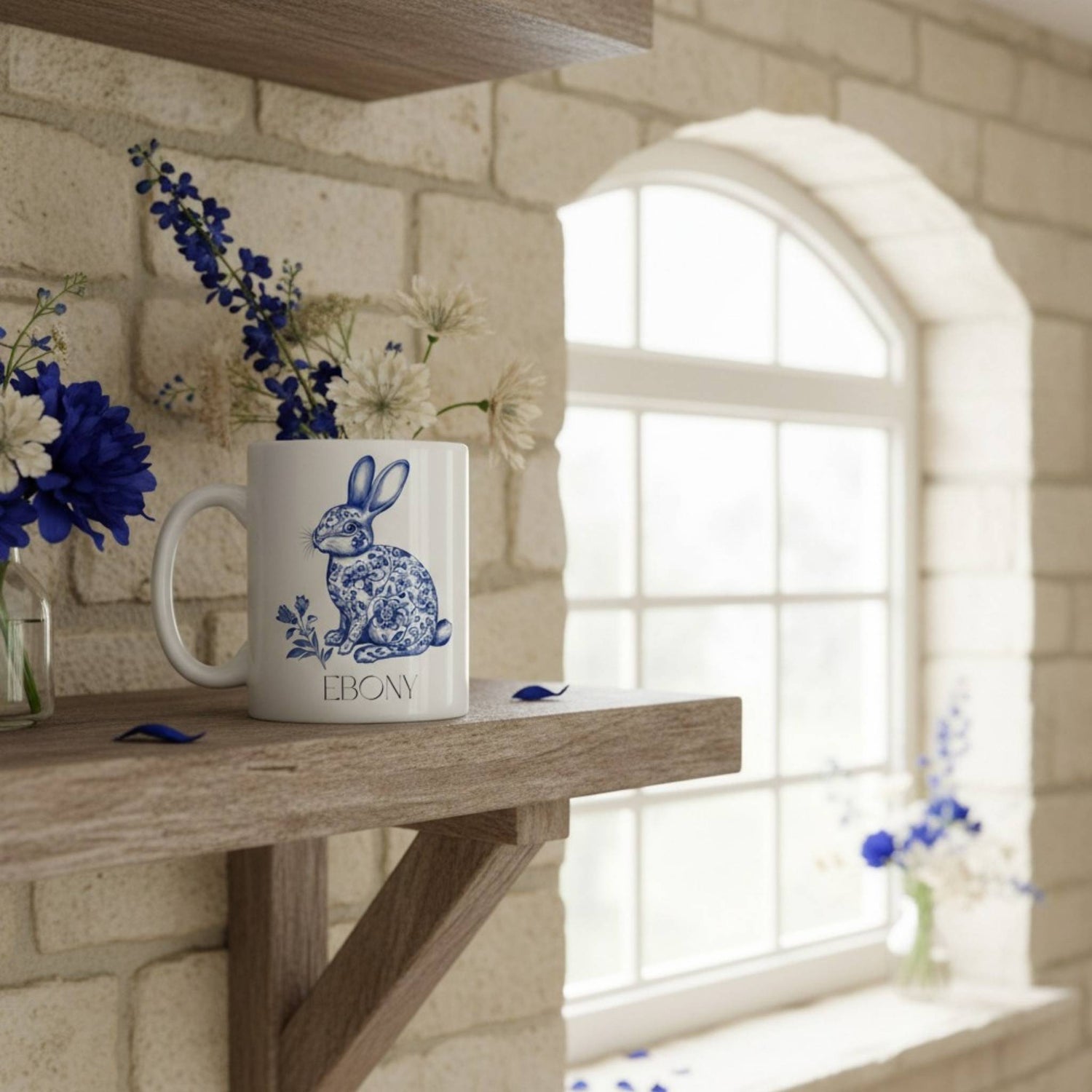 White mug with a hare design on a wooden surface near a window with flowers.