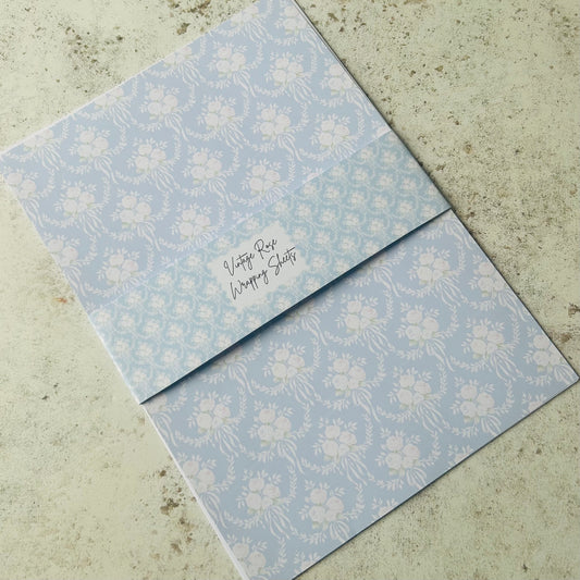 Two light blue floral-patterned wrapping sheets on a concrete surface