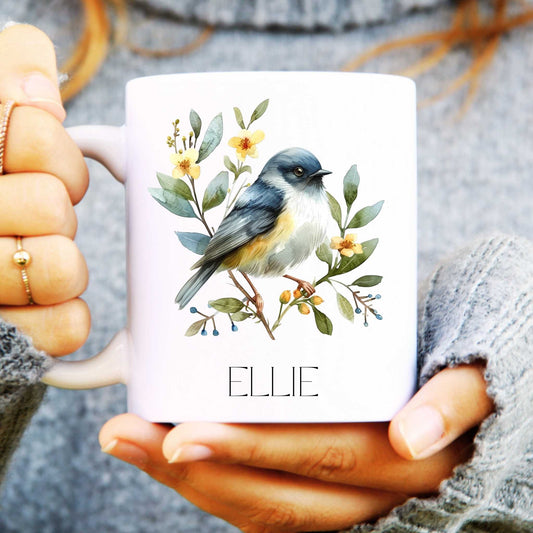 White mug with a bird and floral design held by a person wearing a grey sweater.