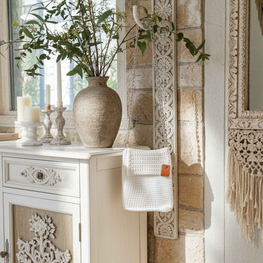Decorative setting with a vase, candles, and a woven bag on a white cabinet.