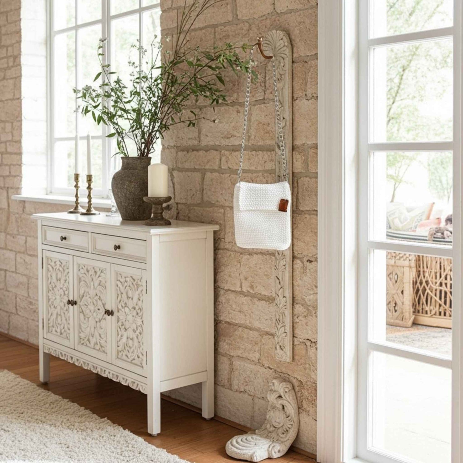 White crochet phone bag next to decorative cabinet with intricate carvings in a room with stone walls and large windows.