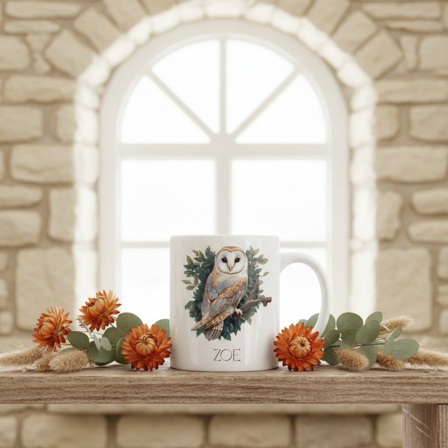 Mug with owl design on a wooden surface with flowers and a stone wall background