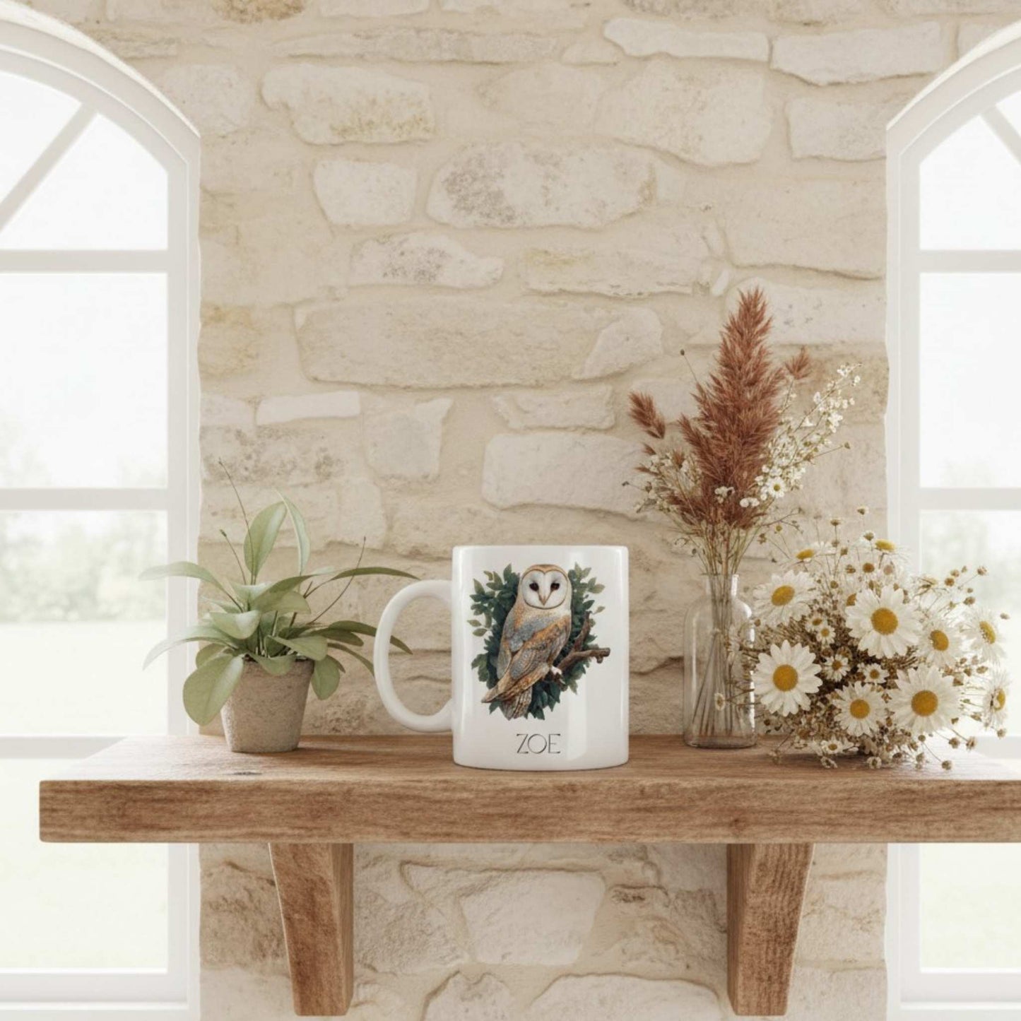 White mug with owl design on a wooden table against a stone wall.