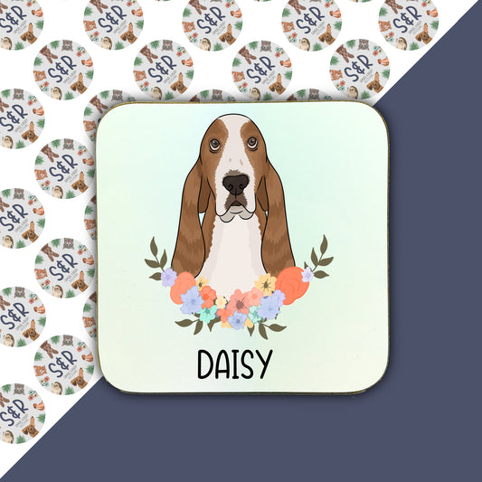 A square coaster with a printed illustration of a basset hound dog surrounded by a floral wreath, with the name 'Daisy' at the bottom.