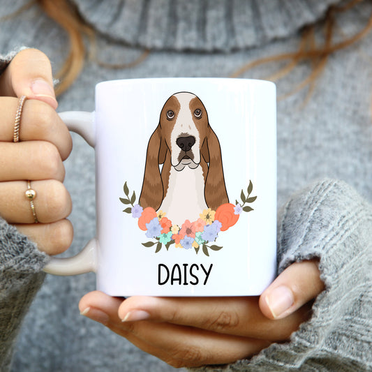 A white ceramic mug with a printed basset hound dog illustration surrounded by a floral pattern, with the name 'Daisy' written on the mug.