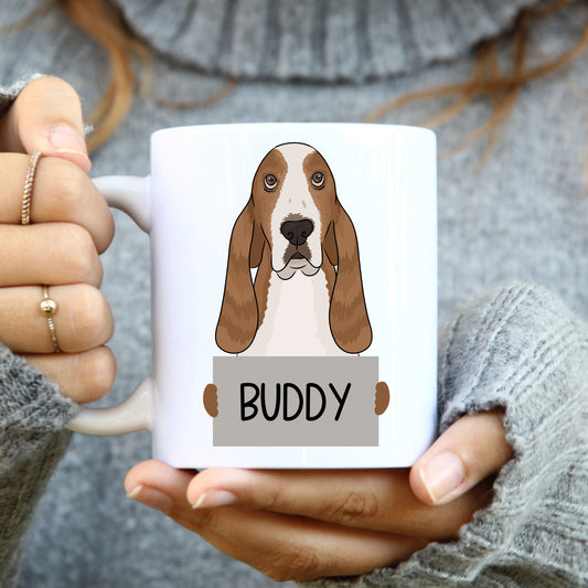 A person holding a white coffee mug with a colourful illustration of a basset hound dog on it.