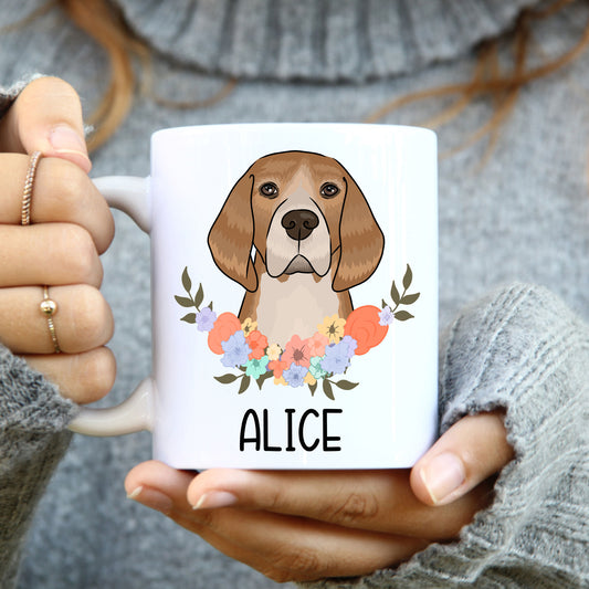 A person holding a white coffee mug with a colourful floral design and a illustration of a beagle dog on the side.