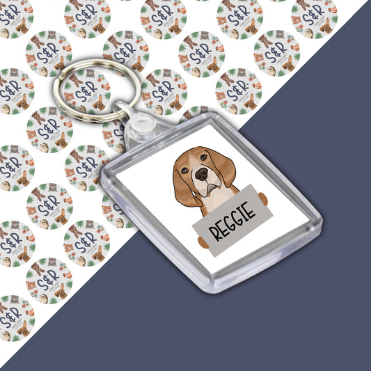 A personalised keyring featuring an illustration of a beagle dog with the name 'Reggie' printed on it, in a clear acrylic case.