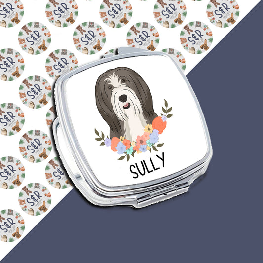 A compact mirror with a personalised design of a bearded collie dog with a floral wreath and the name 'Sully' written on it.