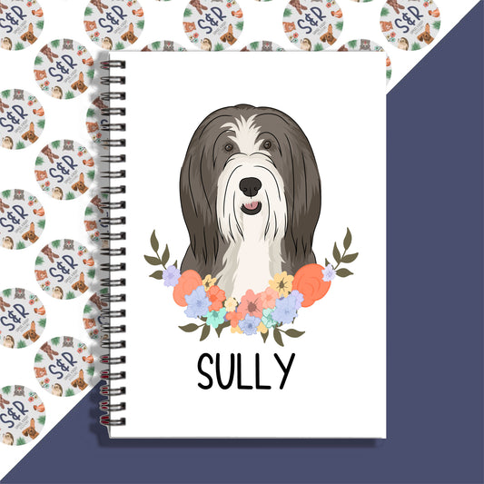 A personalised notebook featuring a graphic of a bearded collie dog on the cover, with a floral pattern in the background.