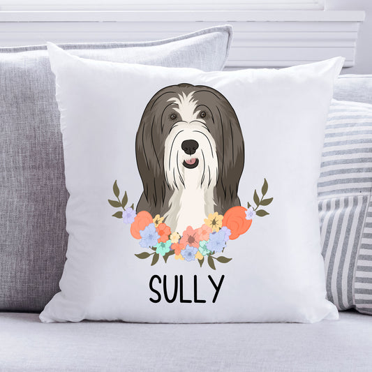 A square-shaped cushion with a printed image of a Bearded Collie dog surrounded by a floral pattern, with the text 'SULLY' on the bottom.