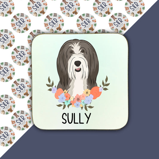 A square coaster with a printed image of a Bearded Collie dog surrounded by a floral pattern.