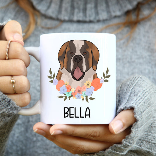 A person holding a white coffee mug with a colourful floral design and a graphic of a Saint Bernard dog.